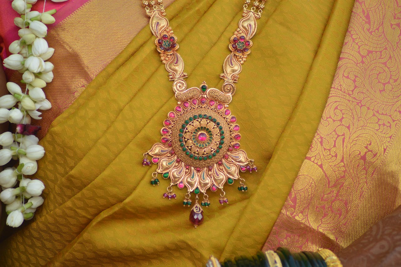 Home Intricate traditional gold necklace with gemstones on vibrant sari fabric.